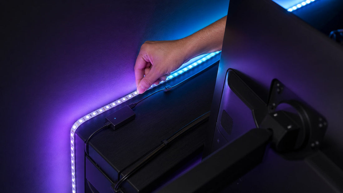 Hand installing an LED strip behind a monitor with purple and cyan bias lighting