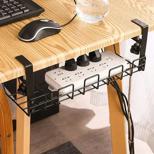 Wire cable tray clamped under a wooden desk holding a power strip and cords