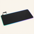 Plain black RGB LED desk mat with illuminated edge, controller and USB cable on a warm off-white background