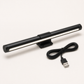Black USB monitor task light with front white LEDs, clip, and cable on a square off-white background